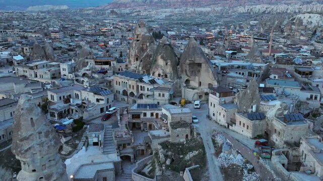 Aerial drone footage of G&ouml;reme town in Cappadocia, Turkey, surrounded by fairy chimneys and volcanic rock formations. The shot reveals traditional stone houses, cave dwellings carved into soft tuff ro