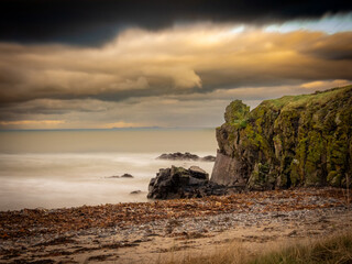 Naklejka premium Machrihanish Beach near Campbeltown.The image is a photograph of a rocky beach with waves under a dramatic, cloudy sky