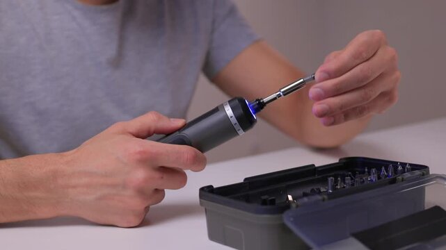 Instructional scene of assembling electric screwdriver bits carefully, Closeup of repair activity involving selecting and installing screwdriver bits on clean table