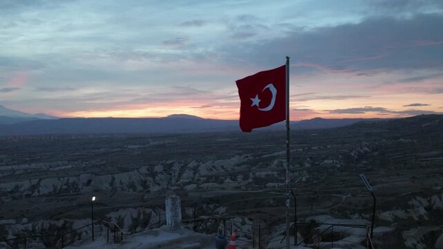 Aerial drone footage of U&ccedil;hisar village in Cappadocia, Turkey, dominated by the iconic U&ccedil;hisar Castle rising above stone houses and cave dwellings. The scene captures the town built into volcanic rock