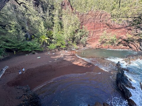 Red sand beach cove with forest cliff and turquoise water