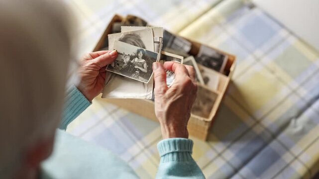 Senior woman looking through old photos from the past, close-up on her hands
