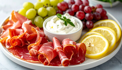 Platter with thinly sliced prosciutto, fresh grapes, lemon slices, cream cheese dip, tasty food, delicious