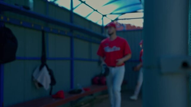The coach greets the baseball players before entering the locker room.. The baseball team sits and chats on the grass.