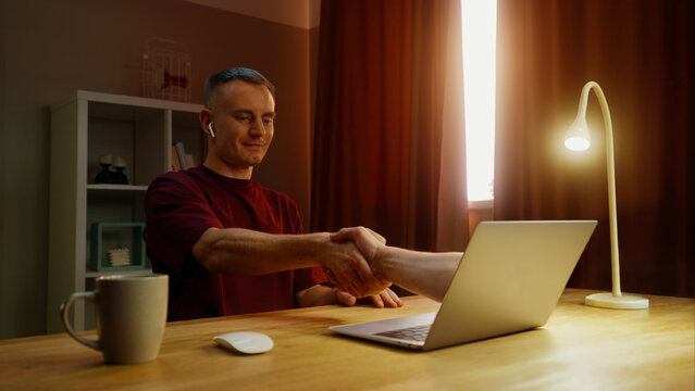 Business man shake hand remotely, handshake through laptop screen. Conclusion agreement at home. Male employee virtual meeting. Successful distant job interview. Guy deal video call. Work conference.
