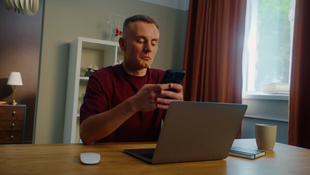 Distracted man worker remote work laptop home. Guy receive cool spicy sms mobile cell phone chatting. Male employee texting message. Ceo person take break rest. Online computer freelance distant job.