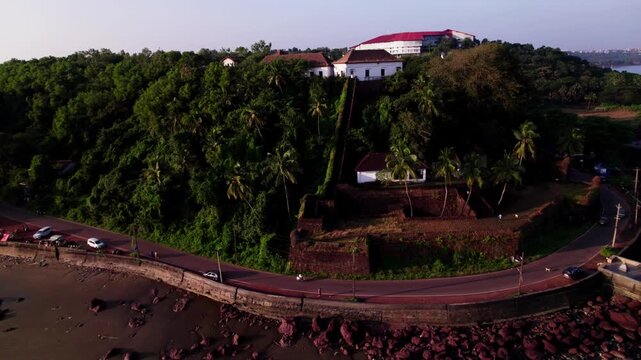 16th-century of historical Reis Magos fort with trees, narrow road and rock beach shoreline at goa, india. day time, push back shot, drone shot, 4k.