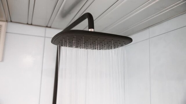 Modern black showerhead releasing water in white tiled bathroom