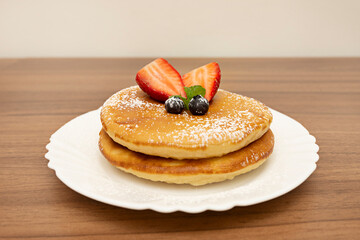 An autumnal still life where the pancakes are presented in a low stack, bathed in compote, with a cinnamon stick and steam rising from the plate.