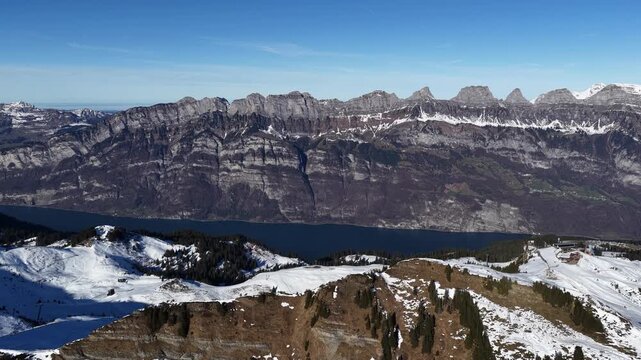 Churfirsten mountain range above Walensee Switzerland with drone slowly moving forward over snowy alpine ridge blue sky dramatic cliffs travel and nature landscape.