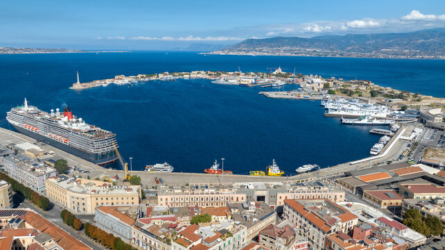 Aerial view of the city port of Messina, Sicily, Italy. Panorama of a crescent-shaped natural harbor. A large cruise ship and various vessels are docked along the quay.The city center is in foreground