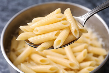 A spoonful of penne pasta being lifted from a stainless steel pot filled with more pasta.