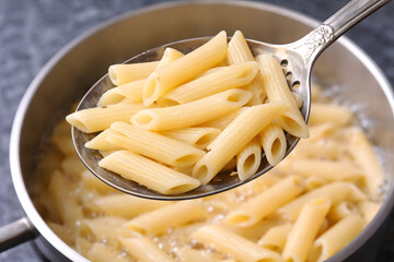 A metal colander with penne pasta over a pot of boiling water on a stovetop