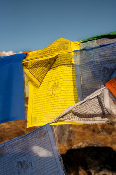 View of vibrant prayer flags fluttering against the stark, clear sky, casting shadows on the rough, rocky ground, Himalaya, Annapurna, Nepal.