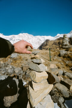 View of a person's hand near a stack of stones overlooking snow-capped mountains against a clear blue sky, Himalaya, Annapurna, Nepal.