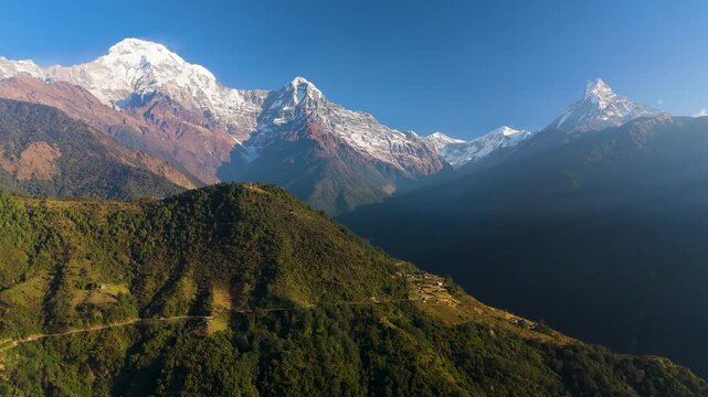 Aerial view of the majestic Annapurna mountains, a dramatic mix of snow-capped peaks and lush green valleys under a clear blue sky, Himalaya, Annapurna, Nepal.