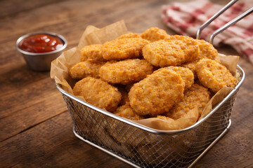 A metal basket filled with crispy chicken nuggets on a wooden table with a side of ketchup