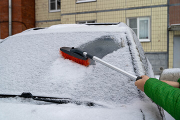 Person clearing snow from a car windshield on a winter day in a city
