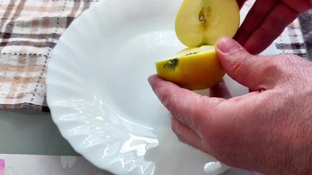 Hands hold a halved yellow apple above a white plate, revealing its fresh core and seeds - capturing a tactile moment in food prep with soft light and a cozy kitchen backdrop