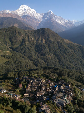 Aerial view of a village nestled among the hills, with snow-capped mountains providing a stunning backdrop, Himalaya, Annapurna, Nepal.