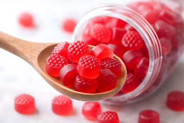 A wooden spoon filled with red gummy bears next to a clear jar