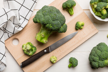 fresh green broccoli on wooden cutting board with knife. Broccoli cabbage leaves. light background. Flat lay
