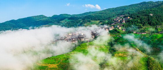Green terraced fields with traditional village shrouded in morning mist and clouds. Famous Longji Rice Terraces natural landscape in Guilin, China.