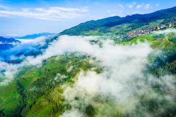 Green terraced fields with traditional village shrouded in morning mist and clouds. Famous Longji Rice Terraces natural landscape in Guilin, China.
