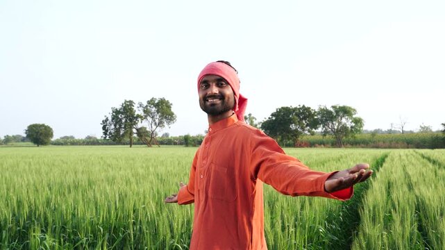 happy indian farmer standing at green wheat field