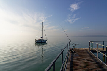 Fototapeta premium Sailboat floating on Balaton under morning light with fishing gear set near the dock