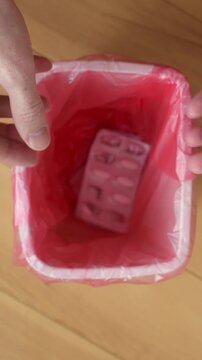 Hands audit home medicine supply, sort blister packs by expiry date and discard outdated tablets into lined trash bin now.