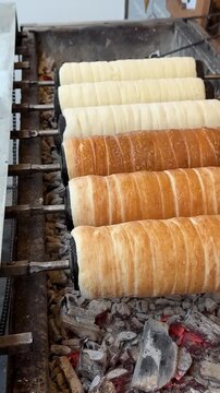 Spinning cylindrical trdelnik dough slowly browning on grill, transforming into golden crispy pastry through traditional czech cooking method over warm coals vertical footage