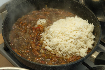 Asian food. Cooking stir fry in wok black pan on the stove. Hot frying beef meat, with onion, soy sauce, red bell pepper, rice. Stir fried dish, releasing steam. Market cooking style. Culinary video