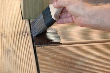 Brown oil for protection of wood by staining. Painting a larch for protecting and pests. Woodworker applying finish to terrace deck board. Repairman varnishing with brush wooden plank floor surface.
