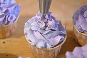 Person decorating cupcakes. Baker piping swirl of a creamy blue purple frosting onto a freshly baked cupcake. Decorated cakes with colorful sprinkles. Sweet Dessert Preparation. Pastry small business