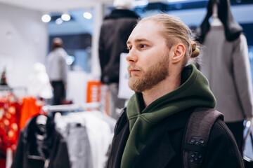 Obraz premium Young bearded man standing in a clothing store, browsing fashion items.