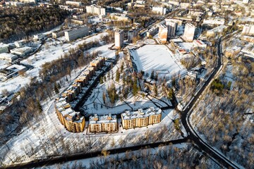 Stunning winter aerial view showcasing a modern curved residential complex nestled amidst snow-dusted trees and urban buildings. Obninsk, Russia