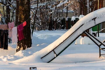 Deserted children's slide blanketed by fresh, pristine snow, glowing under soft winter sunshine. A silent, frosty scene, evoking peaceful cold