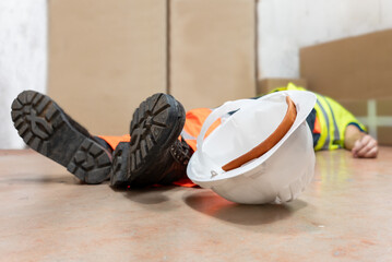 Construction worker lying unconcious on the ground after a workplace accident. Occupational risk prevention. Personal protective equipment (PPE) for health and safety at work.
