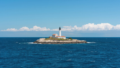 Fototapeta premium Lighthouse on rocky island with blue sea and sky, calm scenic coastal view