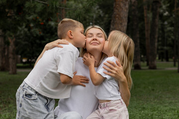 Fototapeta premium A happy mother with two children. A little son and daughter kissing their mother. The concept of happy motherhood and family support.