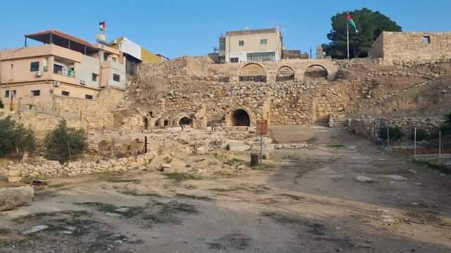 Shot of ancient ruins in the center of Madaba, Jordan, on a bright sunny day, with two Jordanian flags swaying in the breeze under a blue sky and a stray dog nearby
