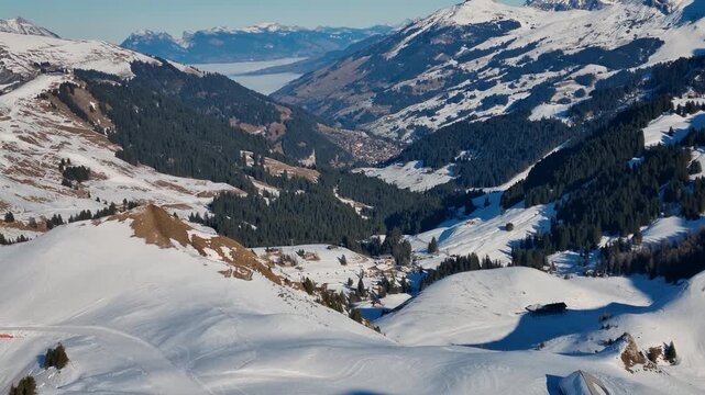 View from B&uuml;hlberg over the Adelboden Valley toward fog-covered Lake Thun on a crisp winter day, framed by snow-covered mountains, showcasing the serene Swiss alpine landscape