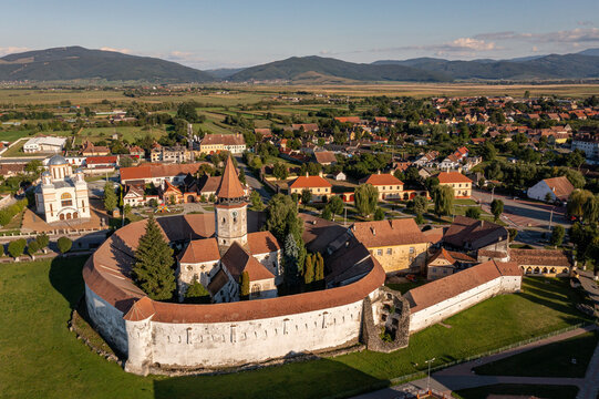 Aerial view of the Prejmer fortified church standing sentinel, its ancient walls a tapestry of weathered stone against the emerald fields, Prejmer, Brasov, Romania.
