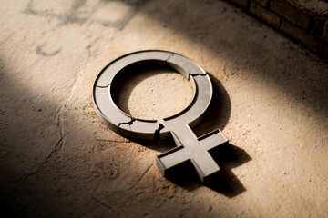 Broken female gender symbol on concrete floor representing femicide