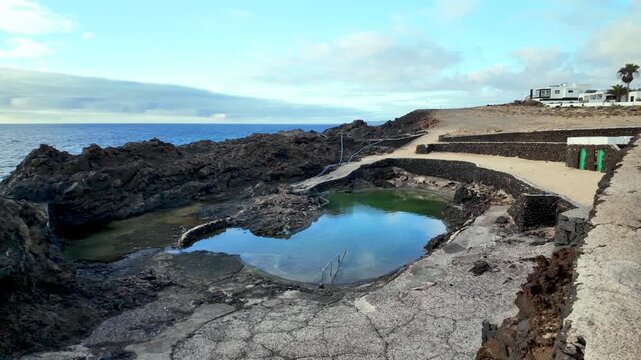 Scenic view of the natural and public swimming pools created by volcanic lava at Charco del Palo, a nudist resort village on the coast of Lanzarote, Canary Islands, with ocean in the background