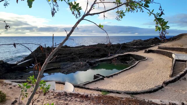 Scenic view of the natural volcanic pools and sandy beach at the nudist resort of Charco del Palo in Lanzarote, Canary Islands, Spain, with the Atlantic ocean in the background