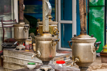 Three antique samovars showcase intricate designs with visible spigots and handles. Nostalgic setting features a small bowl and jar beside them.