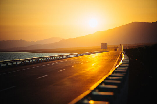 Vehicles driving on a lakeshore road leading to the mountains at sunset, China