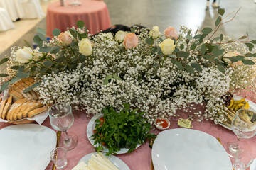 Table setup for a festive gathering with flowers and food in a spacious venue during the evening...